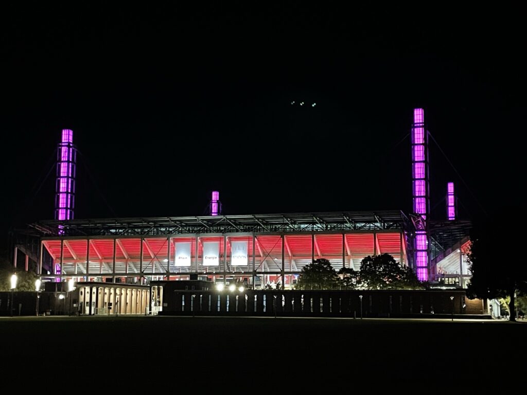 Das RheinEnergieStadion ist nachts in Rot und Lila beleuchtet.